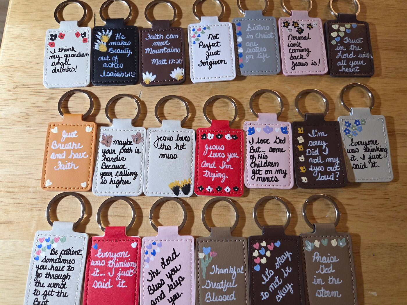 Eighteen hand-painted leather keychains, each lettered with a short verse or encouragement
